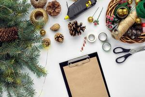 Preparing for Christmas or New Year holiday. Flat-lay of fur tree branches, wreaths, rope, scissors, craft paper over white table background, top view. photo