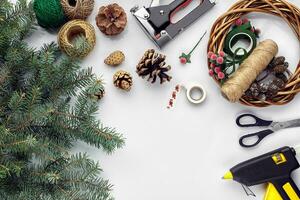 Preparing for Christmas or New Year holiday. Flat-lay of fur tree branches, wreaths, rope, scissors, craft paper over white table background, top view. photo