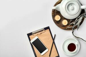 Notebook with craft paper, mobile phone, black tea, glasses on white background with copy space. photo