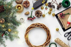 Preparing for Christmas or New Year holiday. Flat-lay of fur tree branches, wreaths, rope, scissors, craft paper over white table background, top view. photo