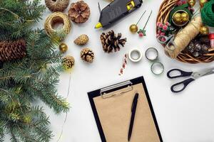 Preparing for Christmas or New Year holiday. Flat-lay of fur tree branches, wreaths, rope, scissors, craft paper over white table background, top view. photo