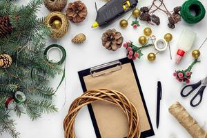 Preparing for Christmas or New Year holiday. Flat-lay of fur tree branches, wreaths, rope, scissors, craft paper over white table background, top view. photo