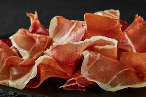 Gourmet, manually sliced jamon on black stone slate board against a dark grey background. Close-up shot. Side view. Copy space. photo