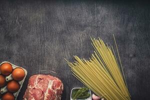 Raw meat beef slices on a wooden cutting board with spaghetti, garlic, spices, peppercorns, salt and dill for cooking pasta. Top view. photo