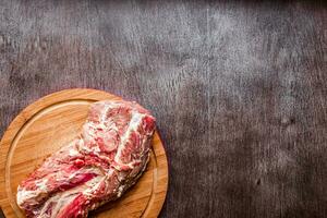 Raw pork on a chopping board on a dark wooden surface. Food background with copy space. Toned photo