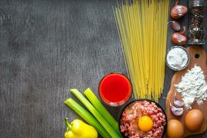 Ingredients for cooking pasta. Spaghetti, tomato juice, olive oil, garlic, minsed meat, pepper and fresh celery on wooden background, top view, copy space photo