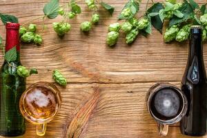 Bottle and a glass of light and dark beer with hops and copy space area on wooden background. Top view photo