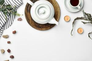 A white porcelain teapot on a wooden board and a white cup with tea on a table. Top view. Copy space. photo