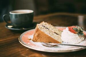 Piece of cake with strawberry and cup of coffee on the wooden table photo