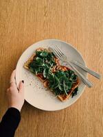 Woman's hand holding a plate of toasted bread with spinach. photo