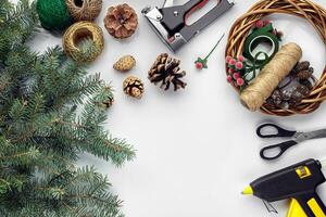 Preparing for Christmas or New Year holiday. Flat-lay of fur tree branches, wreaths, rope, scissors, craft paper over white table background, top view. photo