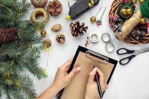 Preparing for Christmas or New Year holiday. Flat-lay of fur tree branches, wreaths, rope, scissors, craft paper over white table background, top view. photo