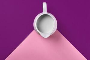 White ceramic jug of fresh milk on purple and pink background. Top view photo