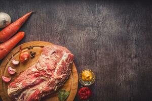 Raw pork on a chopping board on a dark wooden surface and spice for cooking. Food background with copy space. Toned photo