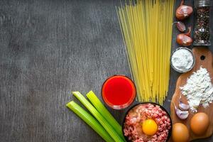 Ingredients for cooking pasta. Spaghetti, tomato juice, olive oil, garlic, minsed meat, pepper and fresh celery on wooden background, top view, copy space photo