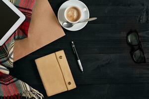 Above view of tablet with notebook and cup of latte coffee on black wooden background. photo