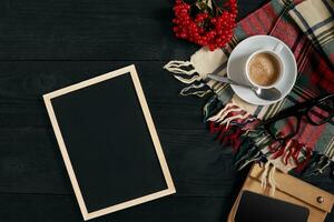 café taza, bufanda en un jaula, cuaderno y teléfono en de madera mesa. parte superior ver con pizarra para tu texto foto