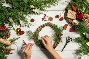 Christmas handmade diy background. Making craft xmas wreath and ornaments. Top view of white wooden table with female hands. photo