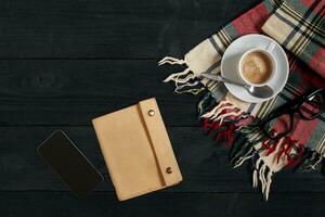 Above view of Smart phone with notebook and cup of latte coffee on black wooden background. photo