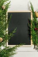 Fir branches border and black chalk board on white wooden background, good for christmas backdrop photo