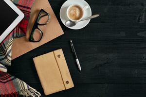 Notebook on wooden table with coffee cup, tablet and glasses beside in morning time photo