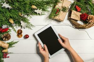 Tablet computer in the human hands. Near the table with tablet computer gift box, christmas bell and fluffy fir branches. photo