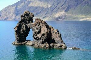 a rock formation in the ocean with a mountain in the background photo