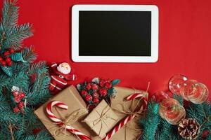 Fir branch, gift box and white tablet with black screen on red background photo