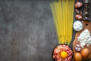 Ingredients for cooking pasta. Spaghetti, eggs, olive oil, garlic, minsed meat, pepper and fresh celery on wooden background, top view, copy space photo