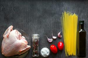 pasta ingredientes. pollo pechos, Cereza Tomates, espaguetis pasta, aceite, especias y ajo en el de madera mesa. espacio para texto. foto