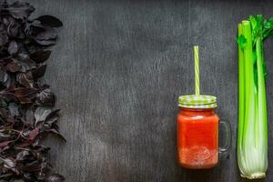 picante tomate bebida con apio y albahaca. tomate bebida en tarro rodeado de Fresco vegetales en un de madera mesa foto