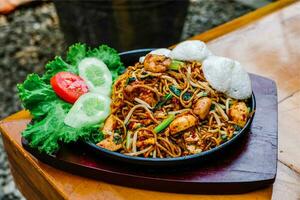 stir-fried noodles with vegetables and shrimp on a black plate on the outdoor photo
