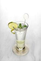 Lemon slush in tall glass with fruit and crushed ice around it on white table with isolated background. Front view. Horizontal composition. photo