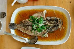 steam fried Marbled Goby fish called Ikan Malas in siamese style served in a dish on a wooden table in a restaurant in Indonesia photo