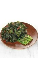 fried cooked green vegetables called kailan are served on a brown wooden plate. isolated on solid white background photo