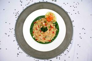 fried rice with vegetables, chicken and chili sauce is served on a white plate on the table photo