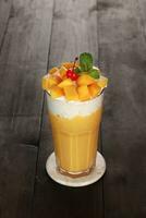 yellow mango juice with garnish of mango pieces, cherries and mint leaves. with a white background and dark wood photo