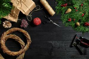 Make a Christmas wreath with your own hands. Spruce branch, Christmas wreath and gifts on a black wooden background photo