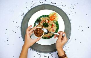 fried rice with vegetables, chicken and chili sauce is served on a white plate on the table photo