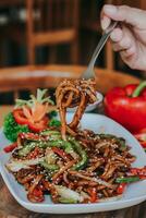 fried udon seafood with vegetables. served in white plate with hand and table of the restaurant photo