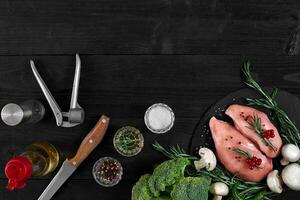 Chicken breast on a cutting board with herbs and different vegetables on rustic wooden background. photo