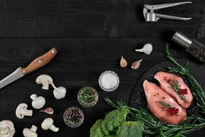 Chicken breast on a cutting board with herbs and different vegetables on rustic wooden background. photo