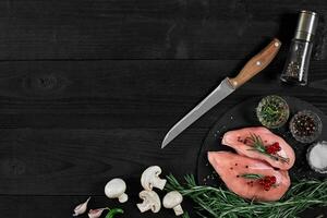 Chicken breast on a cutting board with herbs and different vegetables on rustic wooden background. photo