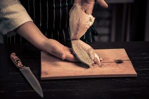 cocinero corte el pescado en un tablero foto