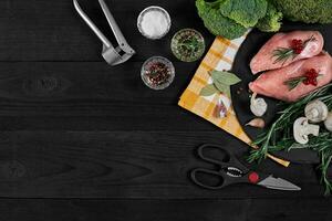 Cooking chicken breasts. On the table are spices - rosemary, red and black pepper, mushrooms, broccoli. Concept - healthy food. photo