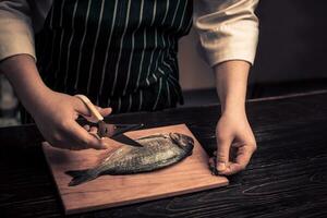 cocinero corte el pescado en un tablero foto