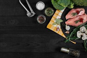 Cooking chicken breasts. On the table are spices - rosemary, red and black pepper, mushrooms, broccoli. Concept - healthy food. photo