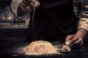 el cocinero rompe huevos dentro un harina en un de madera mesa foto