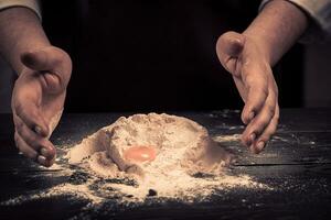 The chef breaks eggs into a flour on a wooden table photo