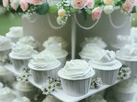 white wedding cake decorated by flowers standing on festive table with lots of snacks on side photo